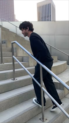 a man in black jacket and pants walking down stairs with skateboard on hand rail