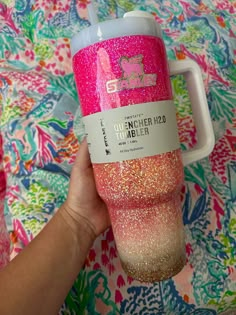 a person holding a pink and gold glitter tumbler cup in their left hand with the lid up