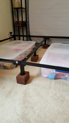 two plastic containers sitting on the floor next to a metal bed frame with white sheets