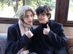 two young men sitting next to each other on a couch giving the thumbs up sign