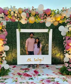 a man and woman standing in front of a photo frame with balloons on the wall