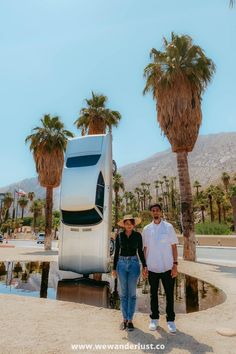 two people standing in front of a truck parked on the side of a road next to palm trees