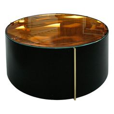 a round glass table with a gold metal bar in the middle and an orange light behind it