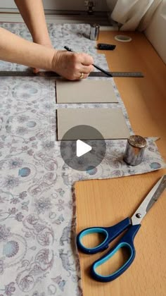 a person cutting up some paper on top of a wooden table with scissors and tape