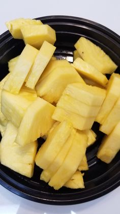 sliced pineapple in a black bowl on a white table