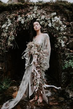 a woman standing in front of a stone wall with flowers and greenery on it