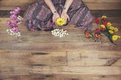 a woman sitting on the floor with flowers around her and petals in front of her