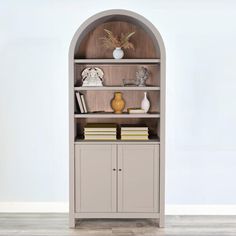 an arched bookcase with books and vases on top, against a white wall