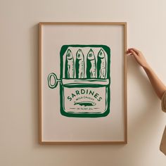 a woman is holding up a green and white poster with some fish in it that reads sardines