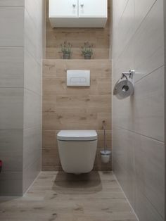 a white toilet sitting inside of a bathroom next to a wooden wall and flooring