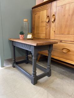 a wooden table sitting on top of a floor next to a dresser and potted plant