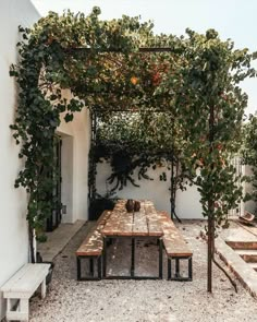 a wooden table sitting under a pergoline covered arbor in front of a white building