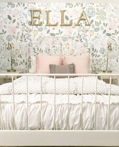 a white bed topped with pillows and blankets next to a wall covered in floral wallpaper