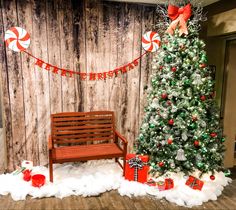 a decorated christmas tree and bench in front of a wooden wall with candy canes