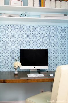 a desktop computer sitting on top of a wooden desk next to a white chair and bookshelf