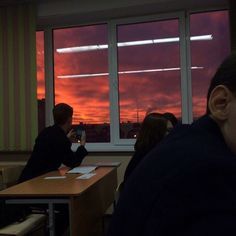 two people sitting at a table in front of a window with the sun going down