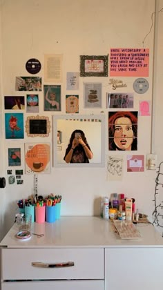 a white desk topped with lots of art and craft supplies next to a wall covered in pictures