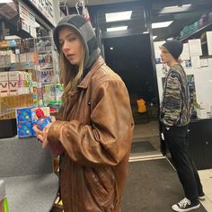 a woman standing in front of a store with a brown leather jacket and hat on