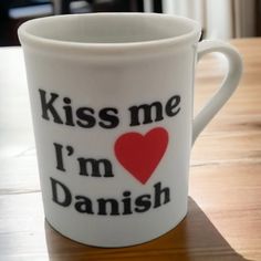 a white coffee mug with the words kiss me i'm danish printed on it