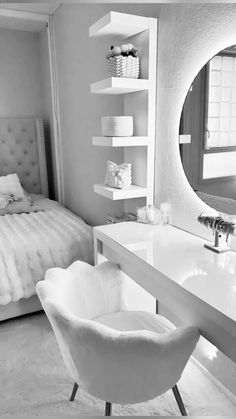 black and white photograph of a bedroom with a bed, chair, desk and mirror