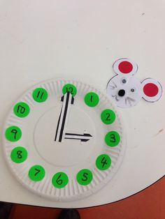 a paper plate clock with green numbers and a mouse on the side next to it