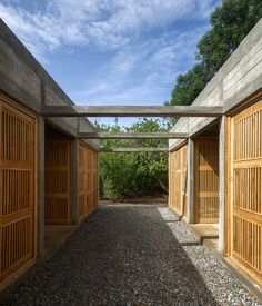 an open walkway between two buildings with wooden doors on each side and gravel ground below