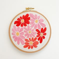 an embroidery project with red and pink flowers on white fabric, framed in wooden hoop