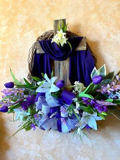 a cross decorated with purple and white flowers in front of a blue scarf on a wall