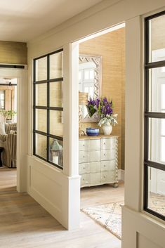 an open door leading to a living room with furniture and flowers in vases on the window sill