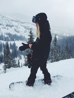 a woman standing on top of a snowboard in the middle of a snowy mountain