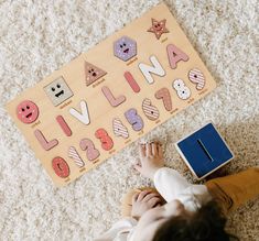 a child laying on the floor next to a wooden puzzle board with letters and numbers