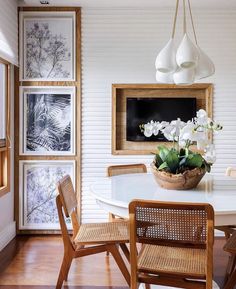 a white dining room table and chairs with pictures on the wall behind it, along with flowers in a basket