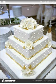 a three tiered wedding cake with white flowers and pearls on the top, sitting on a table