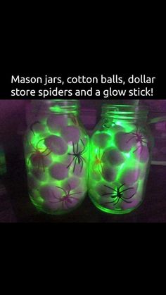 two mason jars with spider webs on them are glowing green and purple in the dark