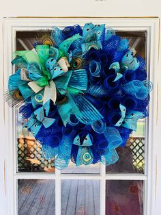 a blue mesh wreath with peacocks and feathers on a window sill in front of a house