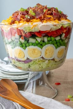 a layered salad with hard boiled eggs, peas and bacon in a large glass bowl