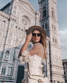 a woman is standing in front of a large building wearing sunglasses and a white dress