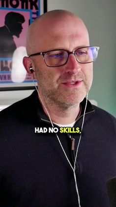 a bald man wearing headphones in front of a poster with the words had no skills