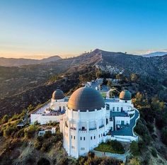 an aerial view of a large white building on top of a hill with mountains in the background