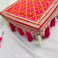 a red and gold table with tassels on it sitting on a white surface