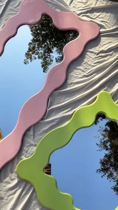 three different colored mirrors sitting on top of a white sheet covered ground next to trees