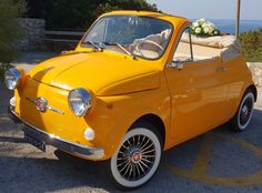 an old yellow car parked on the side of the road with flowers in the back