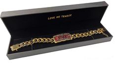 a gold bracelet with red and white stones in a black gift box that says love me tender