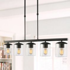 three lights hanging from a ceiling fixture in a room with bookshelves and windows