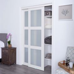 a white closet with frosted glass doors in a room next to a table and chair