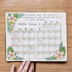 a hand holding a planner with flowers and leaves on the cover, next to a wooden table