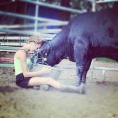 a woman kneeling down next to a black cow