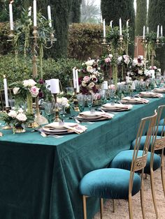 a long table is set with blue velvet chairs and green linens, white flowers are on the tables