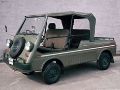 an olive green golf cart is parked in front of a gray wall and there's no door on it