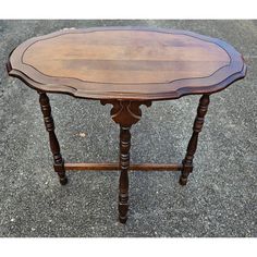 an oval wooden table with turned legs on the top is sitting on concrete and looks like it could be used as a coffee table or side table